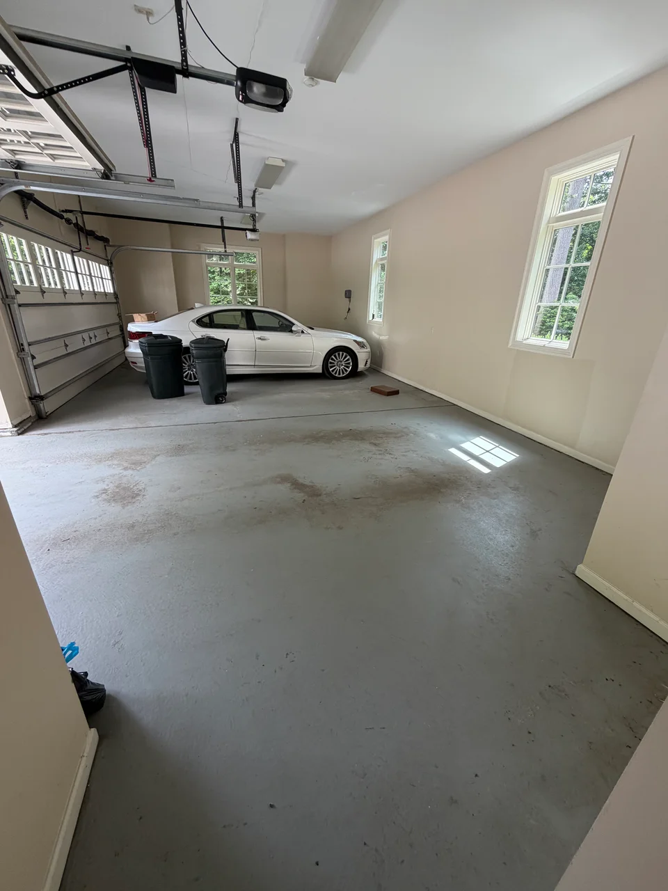 Garage interior before work, with beige walls, bare concrete floor and a parked car